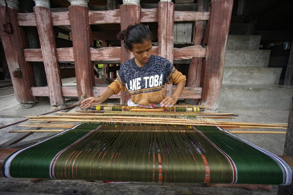 Penenun mengerjakan kain ulos dengan alat tenun tradisional di Samosir